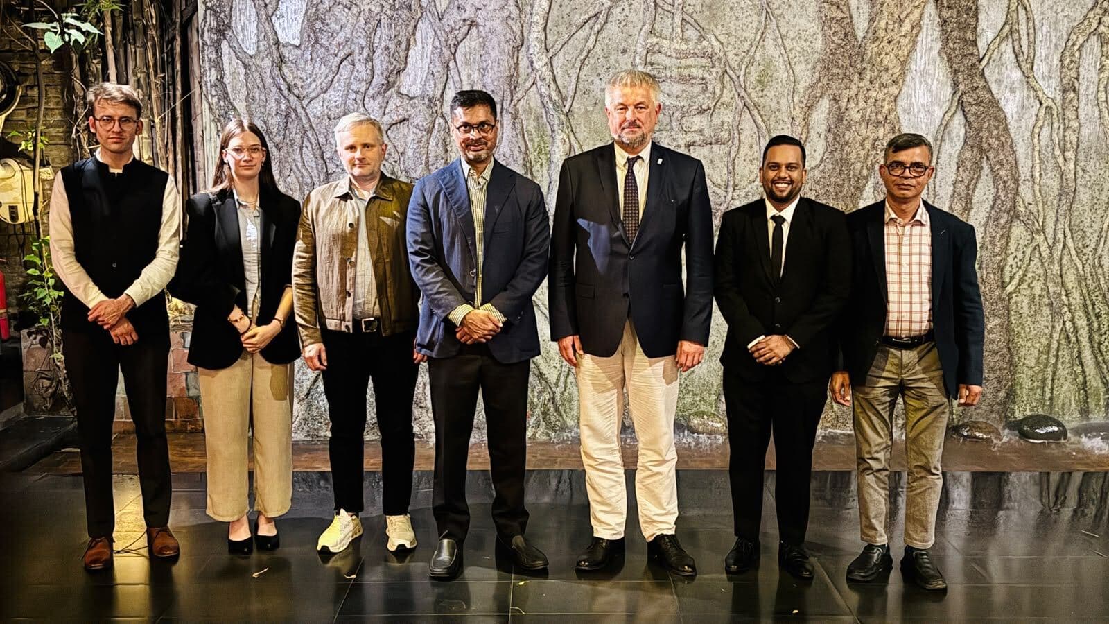 Members of the Lithuanian delegation and Eskimi colleagues standing together in front of a textured stone wall.