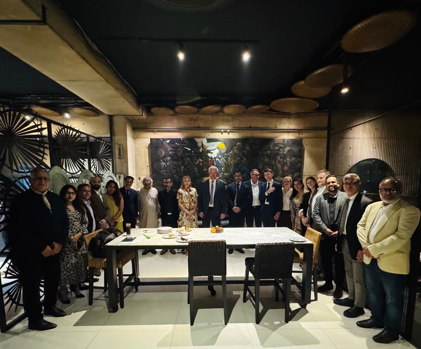 A group of guests standing around a dining table at an evening gathering.